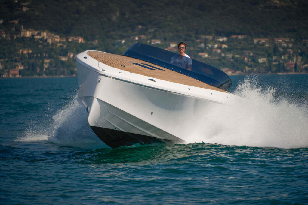 Sportliches Motorboot Frauscher 1212 Ghost in voller Fahrt auf dem Wasser, gesteuert von einem Mann, mit einer landschaftlichen Kulisse im Hintergrund.